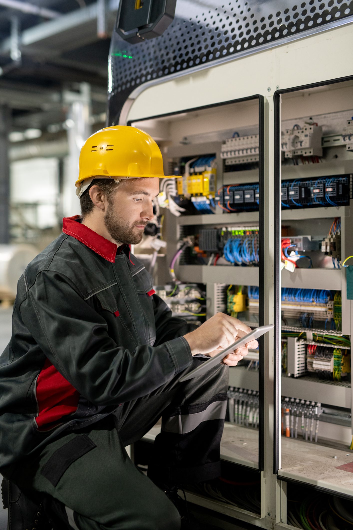 Contemporary young engineer of factory in workwear and hardhat using tablet